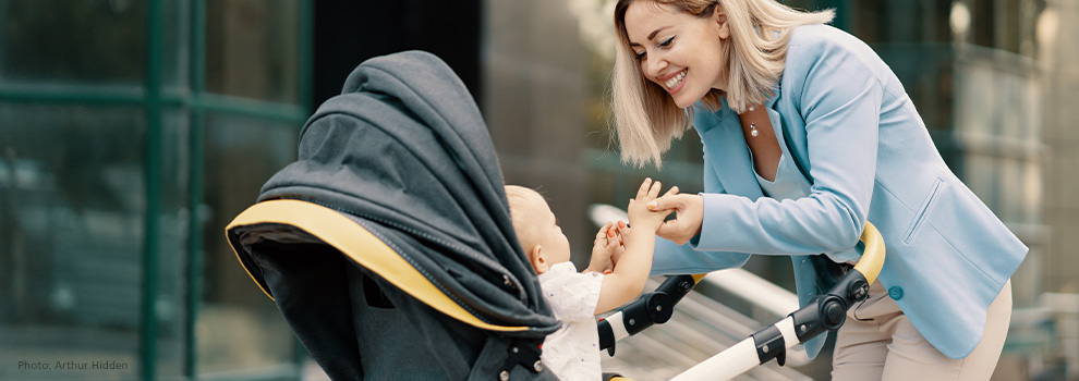 Mutter beugt sich über den Kinderwagen und ihr Baby streckt sich ihr entgegen und ihre Hände zu ergreifen
