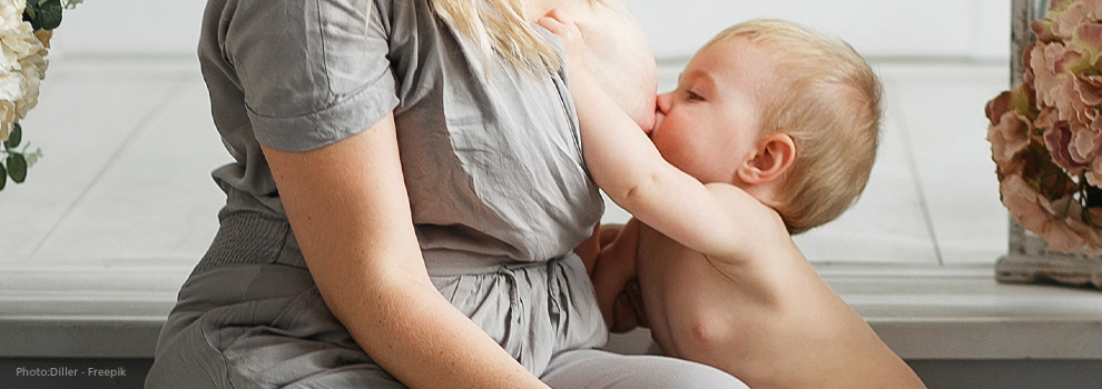 Mutter stillt im Sitzen in Kleinkind. Das Kind greift ebenfalls sitzen vor der Mutter nach der Brust