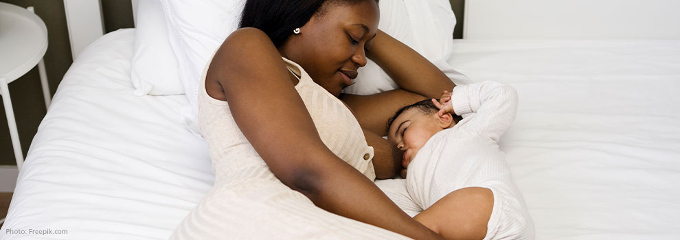 Mutter stillt in Seitenlage und stützt den Kopf auf ihren Arm ab, die andere Hand liegt auf dem Bein des Babys