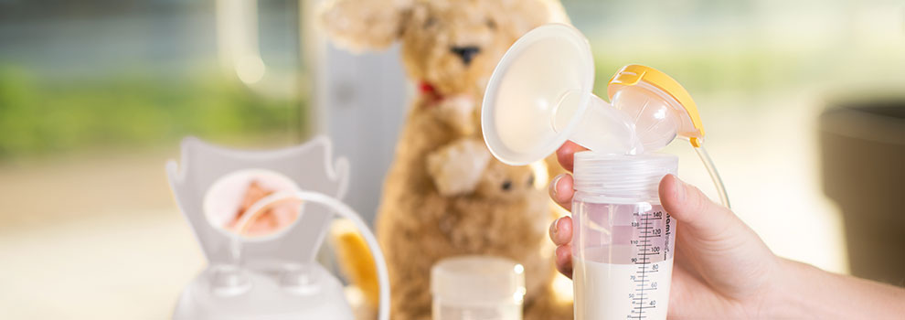 Hand hält mit Milch befülltes Pumpset im Hintergrund die mamivac Lactive und daneben ein Stoffkänguru