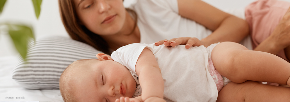 Eine Mutter legt ihre Hand auf ihr schlafendes Baby und schaut es an