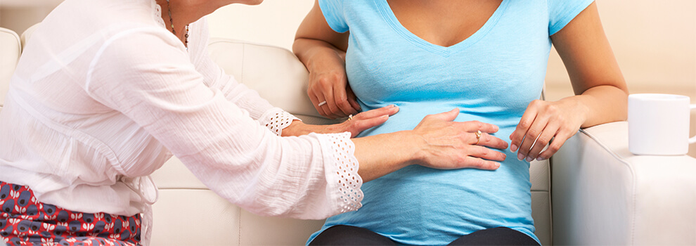 Hebamme tastet den Bauch einer schwangeren Person ab