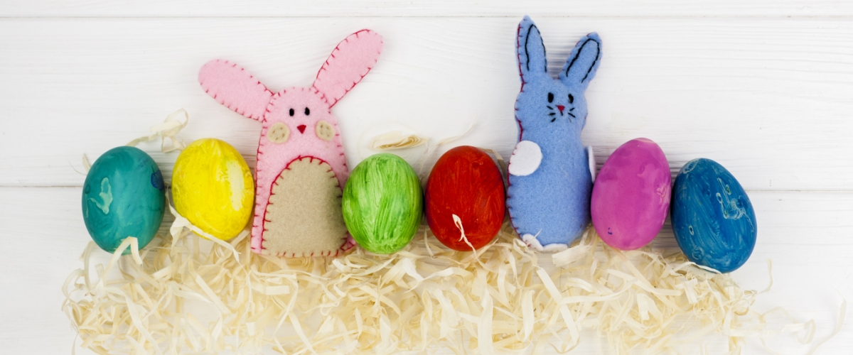 2 selbtgenähte Hasen und bunte Eiere liegen auf Strohbett