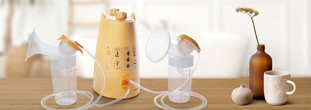 Die elektrische mamivac SENSITIVE-C Muttermilchpumpe, mit 2 Pumpsets steht neben eine Blumenvase auf dem Tisch