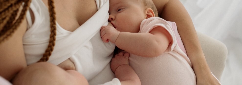 Tandemstillen: Mutter mit geflochtenen Zöpfen gibt ihre Zwillinge zeitgleich beide Brüste